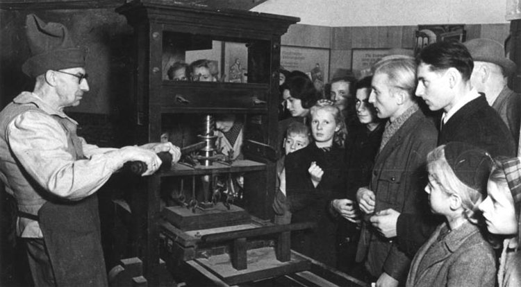Een drukker in oorspronkelijke beroepskleding toont in 1947 hoe de Gutenberg-pers werkt. Foto: © Bundesarchiv
