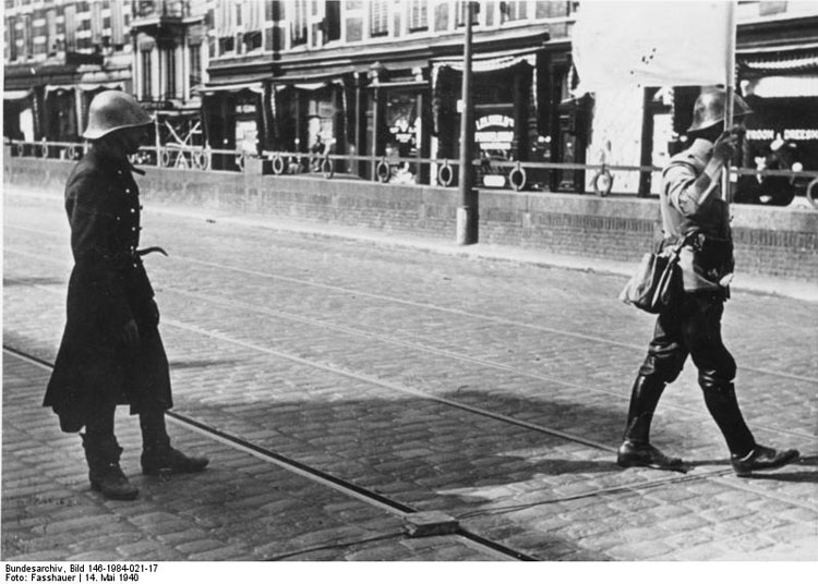 Een Nederlandse onderhandelaar (met de witte vlag) geeft zich op 14 mei 1940 over in de Van der Takstraat in Rotterdam. De Duitsers hebben op dat moment het Noordereiland bezet. © Bundesarchiv
